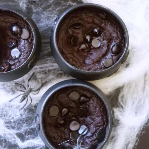 An overhead view looking down onto three cauldron cakes sitting amidst spider webs.