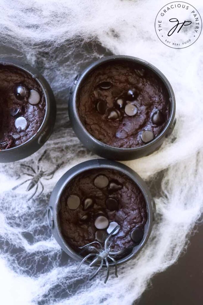 An overhead view looking down onto three cauldron cakes sitting amidst spider webs.