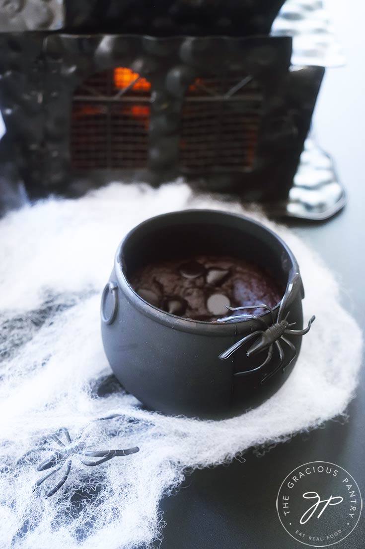 A single cauldron cake with a black spider sits in front of a black haunted house.