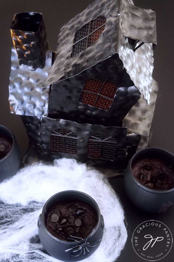 An overhead view looking down on a black haunted house and three cauldron cakes.