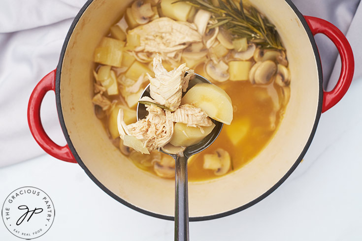 A ladle lifting some Chicken And Parsnip Soup out of a stockpot.