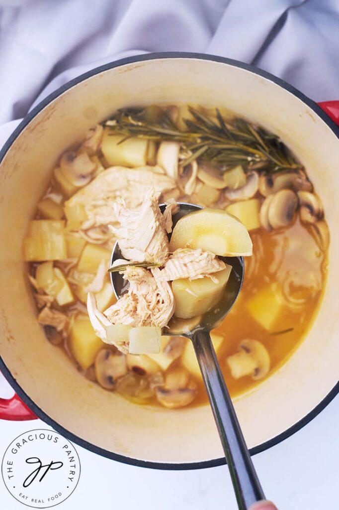 A top view of a ladle lifting some Chicken And Parsnip Soup out of a stockpot.