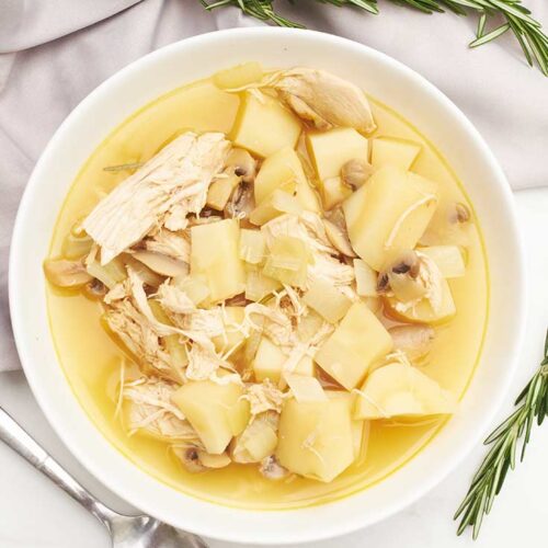 An overhead view of a white bowl filled with Chicken And Parsnip Soup.