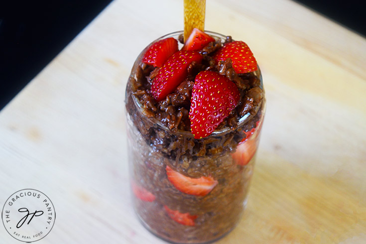 Layered chocolate oatmeal and strawberries in a glass with a wooden spoon.