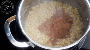 Cocoa powder added to cooked oats in a pot.