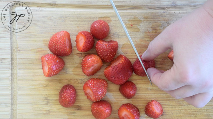 Chopping strawberries on a wooden cutting board.