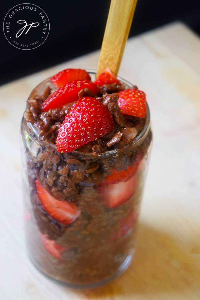 A side view of a glass cup filled with Chocolate Oatmeal and strawberries.