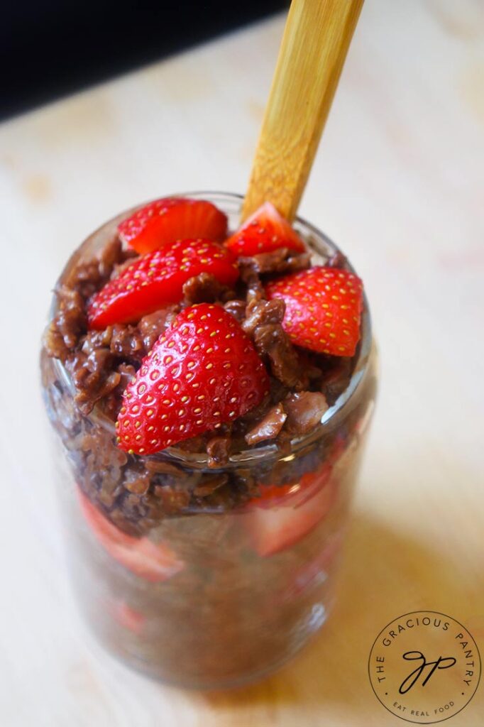 A spoon resting in a full cup of chocolate oatmeal topped with fresh cut strawberries.