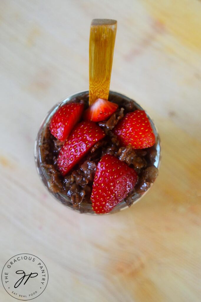 An overhead view looking down into a cup filled with chocolate oatmeal and topped with fresh cut strawberries.