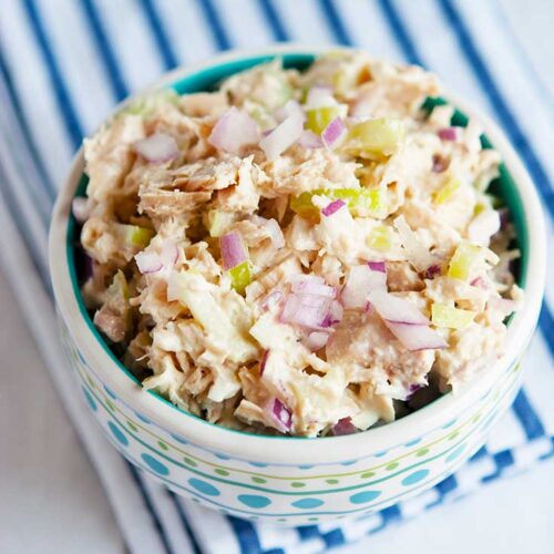 A bowl sitting on a blue stripped towel, filled with Healthy Tuna Salad.