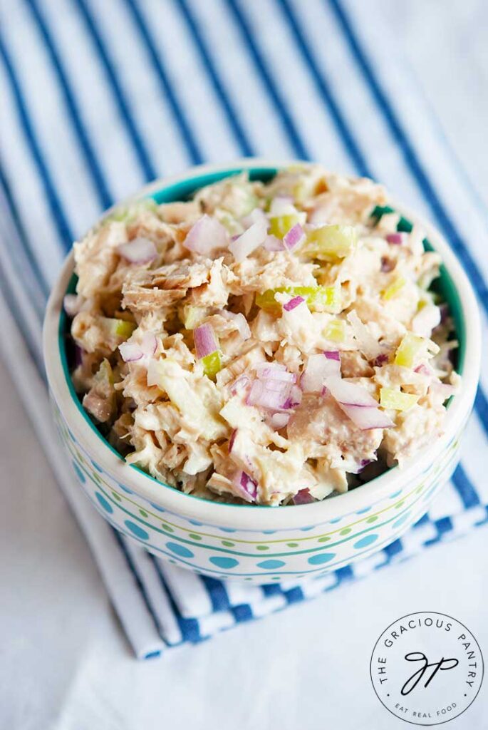 A bowl sitting on a blue stripped towel, filled with Healthy Tuna Salad.