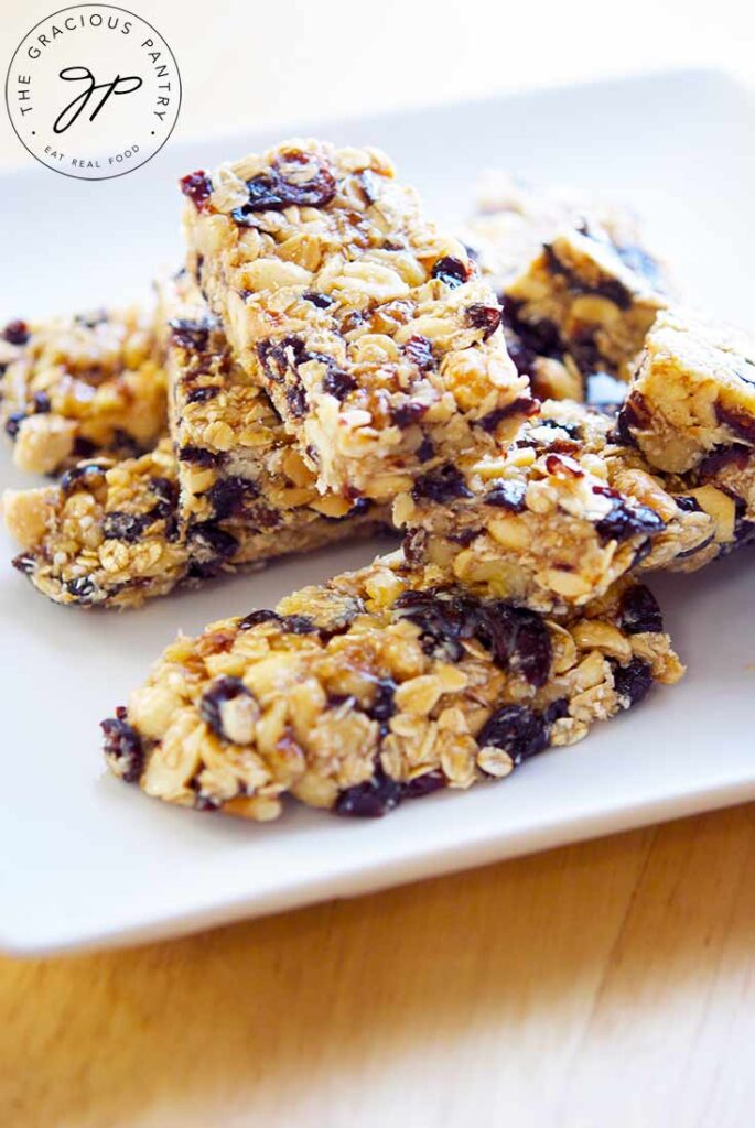 Eight Coconut Granola Bars stacked on a white plate, sitting on a wooden surface.