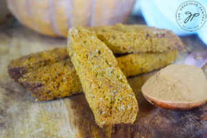 Gluten-Free Pumpkin Biscotti laying on a wooden surface next to a heaping tablespoon of pumpkin pie spice.