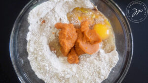 The wet ingredients added to the Gluten-Free Pumpkin Biscotti flour mixture in a mixing bowl.