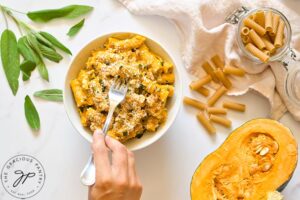 A female hand holding a fork picks up some Pumpkin Pasta out of a white bowl.