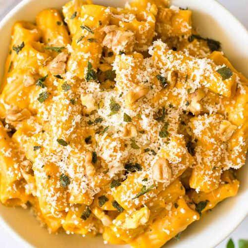 A closeup of Pumpkin Pasta in a white bowl, garnished with parmesan cheese.