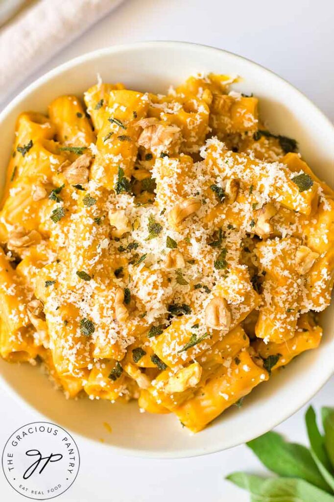 A closeup of Pumpkin Pasta in a white bowl, garnished with parmesan cheese.