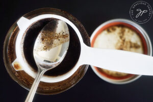 Straining coffee grounds from coffee with a small sieve and spoon.
