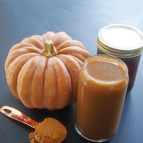 A glass of Pumpkin Spice Cold Brew Coffee sits next to a pumpkin and a tablespoon of pumpkin pie spice.