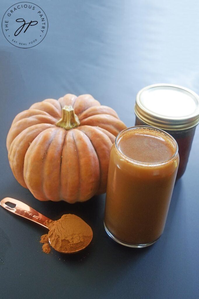 A glass of Pumpkin Spice Cold Brew Coffee sits next to a pumpkin and a tablespoon of pumpkin pie spice.