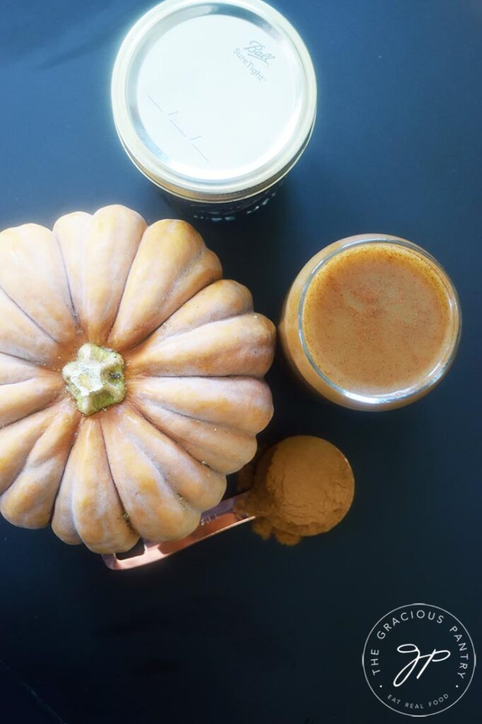 An overhead view of a glass of Pumpkin Spice Cold Brew Coffee, a pumpkin, a canning jar and a measuring spoon with pumpkin pie spice.