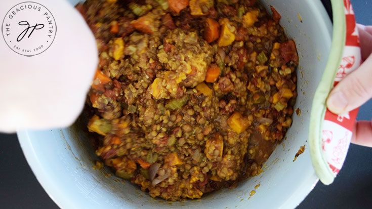 Stirring Slow Cooker Lentil Stew in a slow cooker crock after cooking.