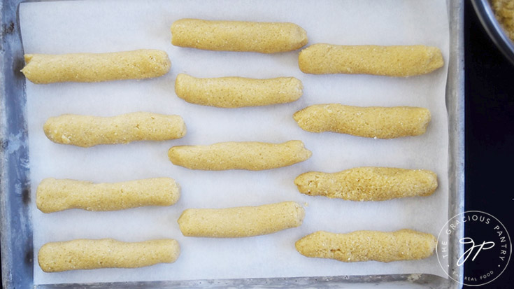 Little sausages of dough laid out on a parchment-lined cookie sheet.