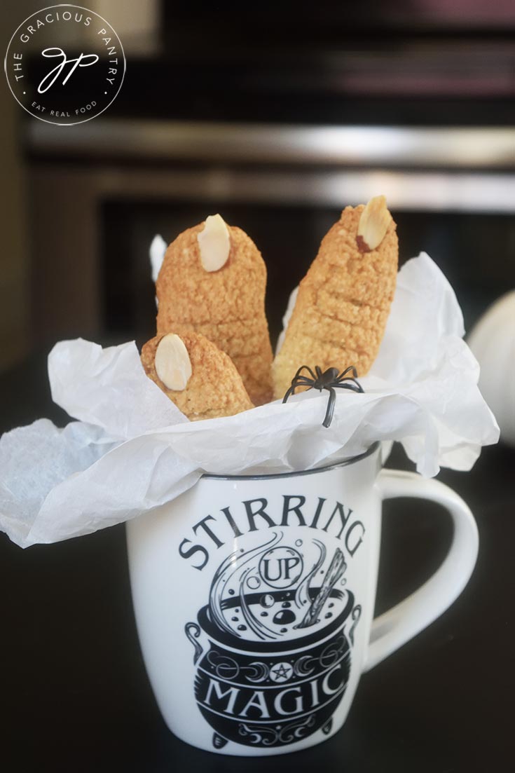 A side view of a halloween mug holding three witch finger cookies.