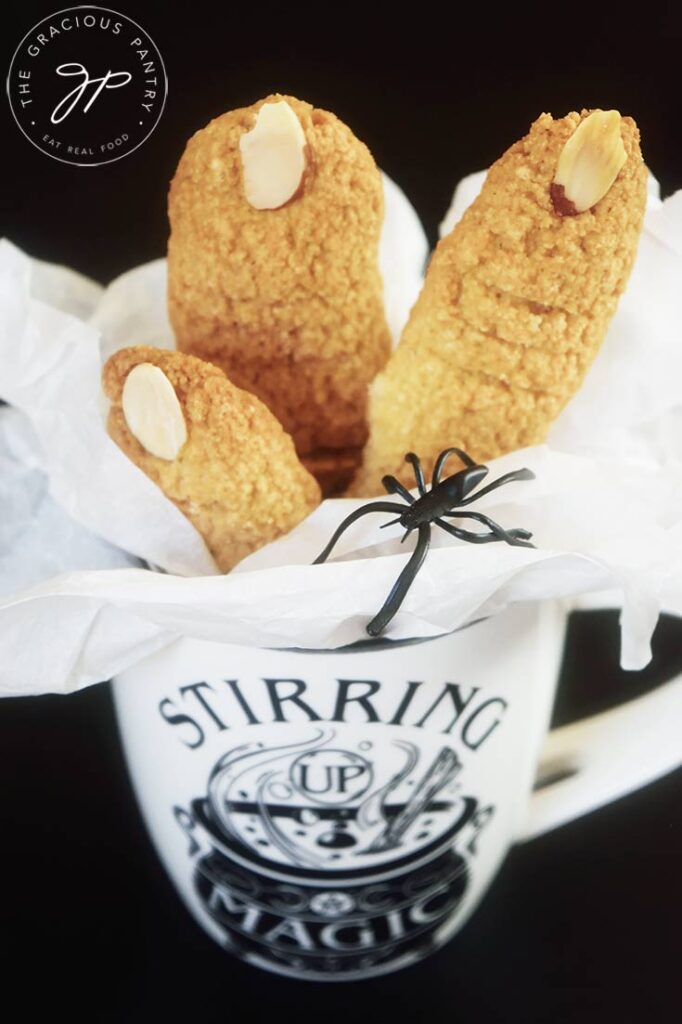 A close up side view of three witch finger cookies in a halloween mug.