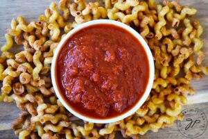 Air Fryer Pasta Chips surrounding a white bowl filled with marinara sauce.