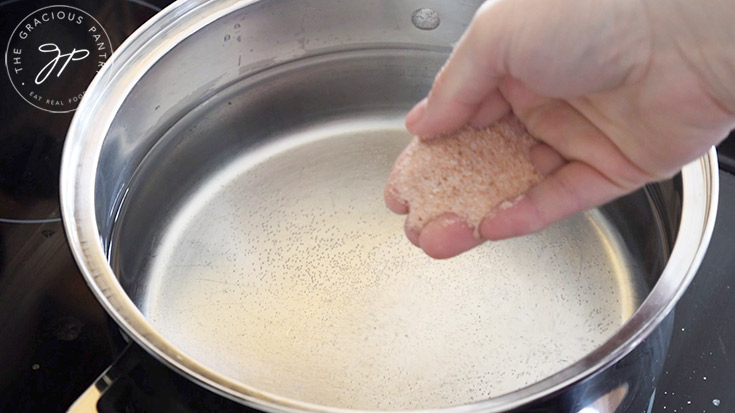 Adding salt to pasta water in a large pot.