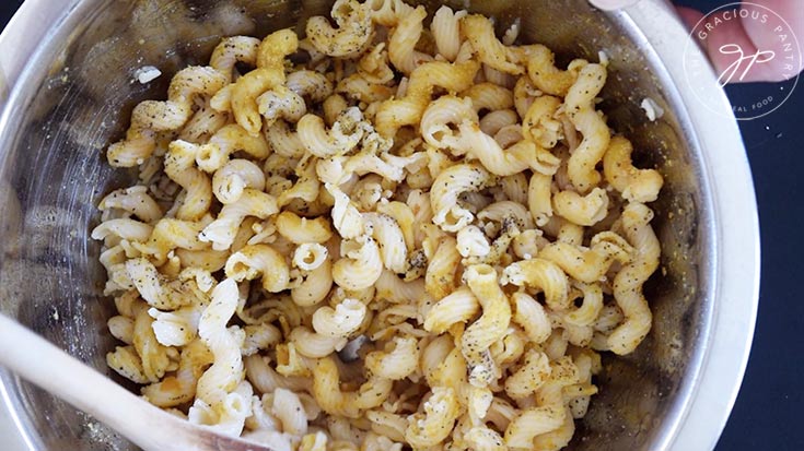 Stirring pasta with oil and seasoning in a mixing bowl.