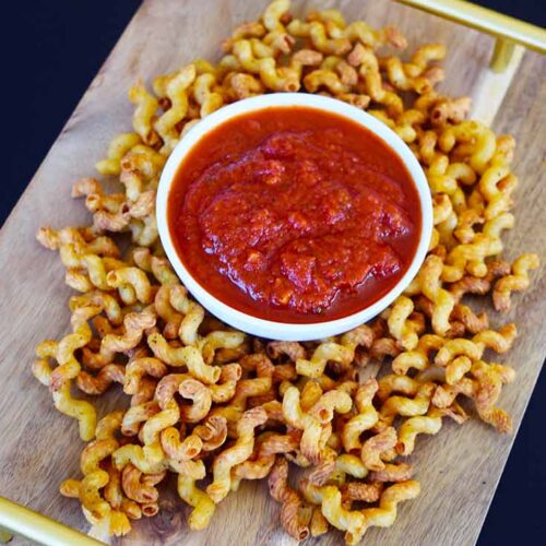 Air Fryer Pasta Chips surrounding a white bowl of marinara on a cutting board tray.