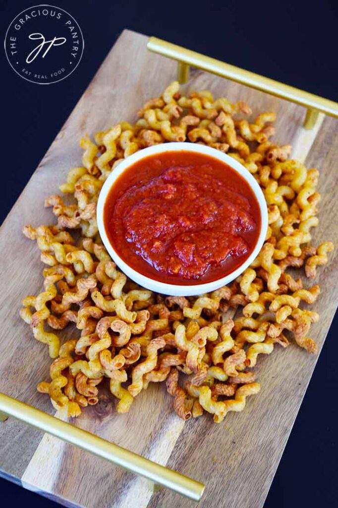 Air Fryer Pasta Chips surrounding a white bowl of marinara on a cutting board tray.