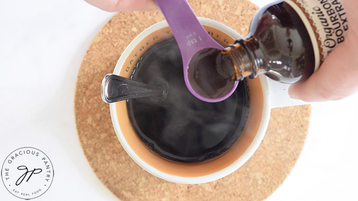 Measuring a teaspoon of vanill extract into a cup of coffee.