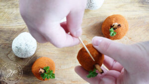 Gently pressing a toothpick into the side of a cheese ball to make the indents of a pumpkin.
