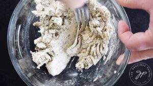 A fork mixing ranch mix into cream cheese in a mixing bowl.