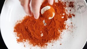 A small cheese ball being rolled in paprika.