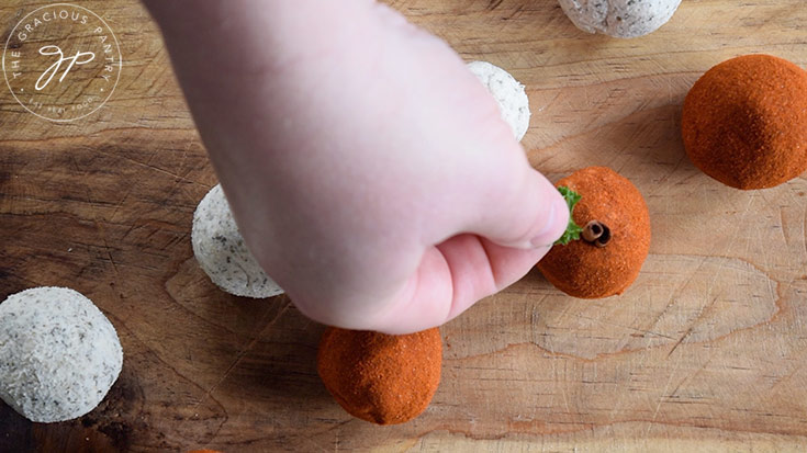 Pressing a small cinnamon stick and parsley sprig into a small cheese ball.