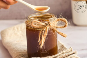 A small white spoon lifts some homemade fish sauce out of a full jar.