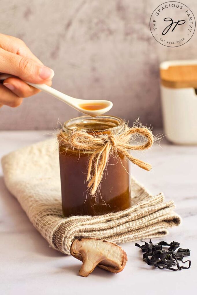 A side view of a small, white spoon lifting some homemade fish sauce out of a full jar.