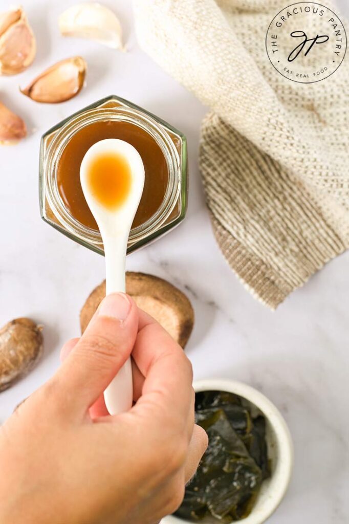 And overhead view of a white spoon lifting some homemade fish sauce out of a glass jar.