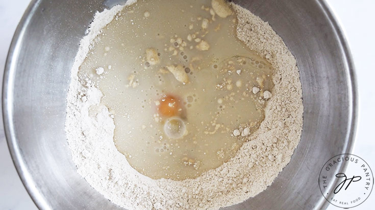 Eggs and milk added to a flour mixture in a metal mixing bowl.