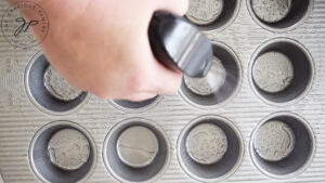 Spraying oil on a muffin pan with an oil sprayer.