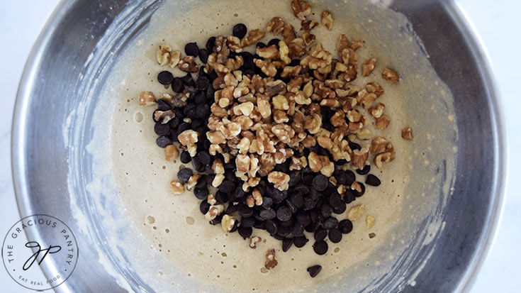 Chocolate chips and walnut pieces sitting in pancake batter in a mixing bowl.