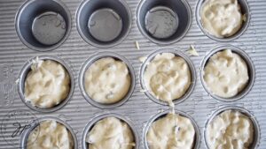 A muffin pan filled most of the way with pancake muffin batter. 3 wells remain empty.