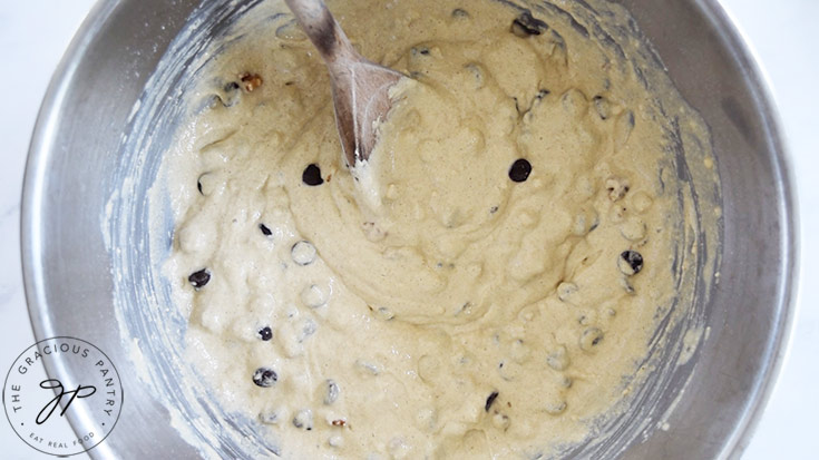 Just-mixed pancake muffin batter with chocolate chips and walnut sitting in a metal mixing bowl.