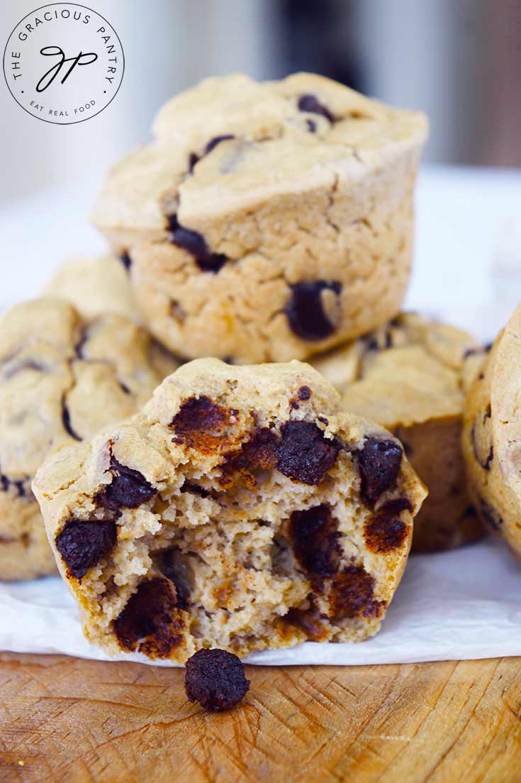 A stack of Pancake Muffins sit behind a single Pancake Muffin that has been cut in half showing all the chocolate chips inside.