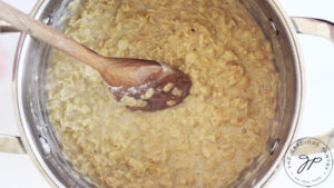 Cooked oats with a wooden spoon sitting in the pot.