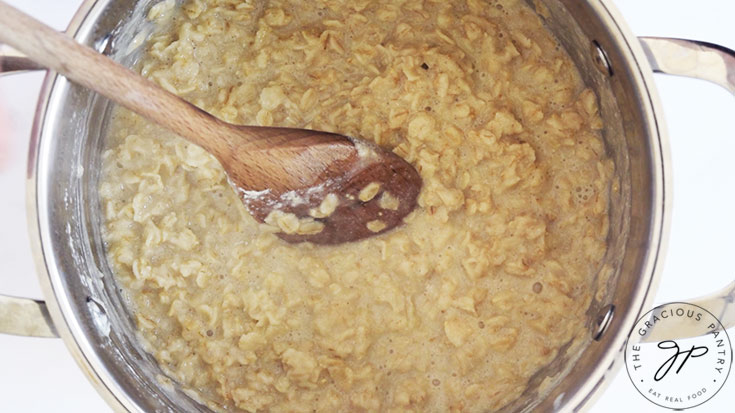 Cooked oats with a wooden spoon sitting in the pot.